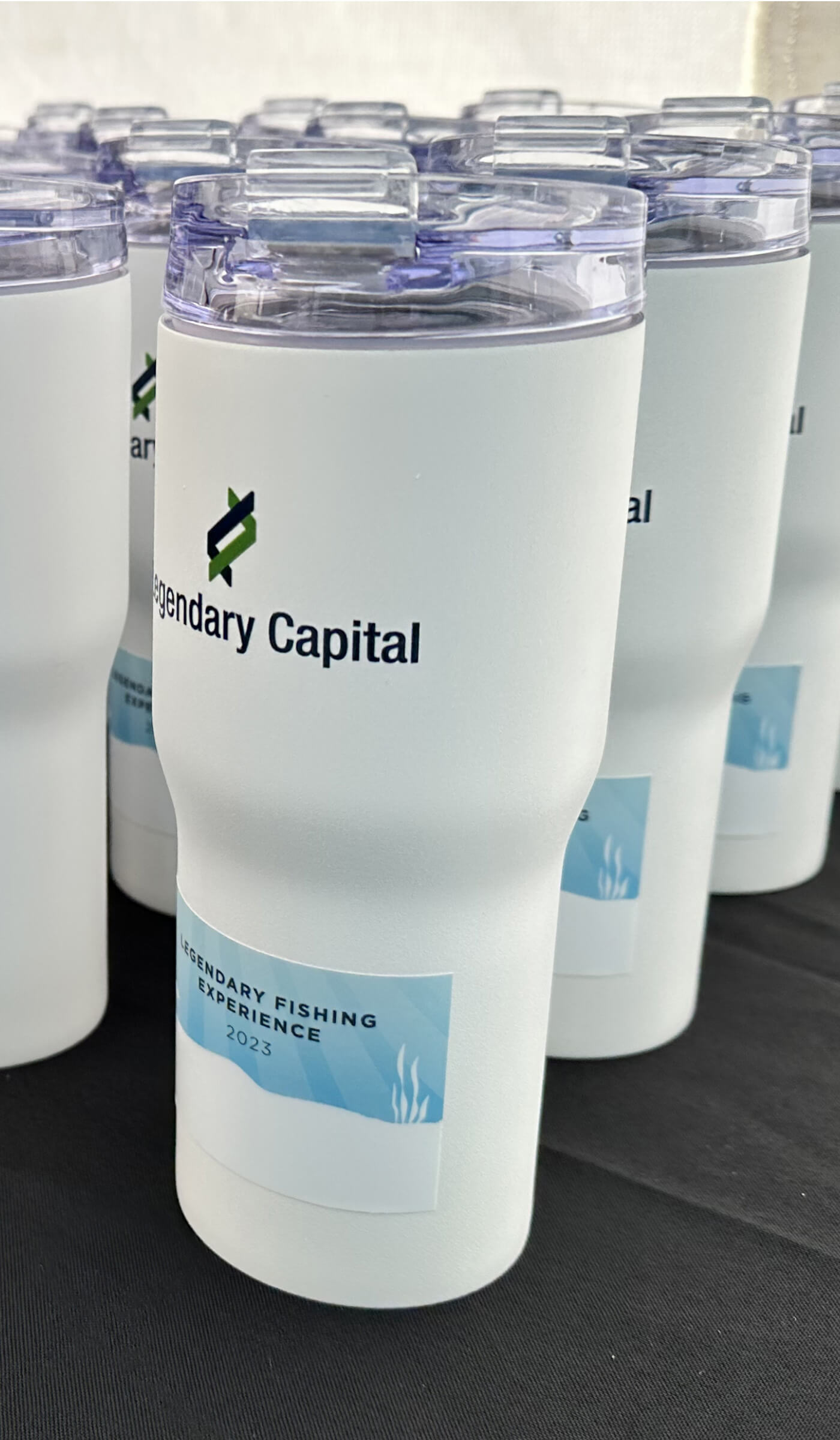 A group of white tumbler cups with the company logo and event sticker.
