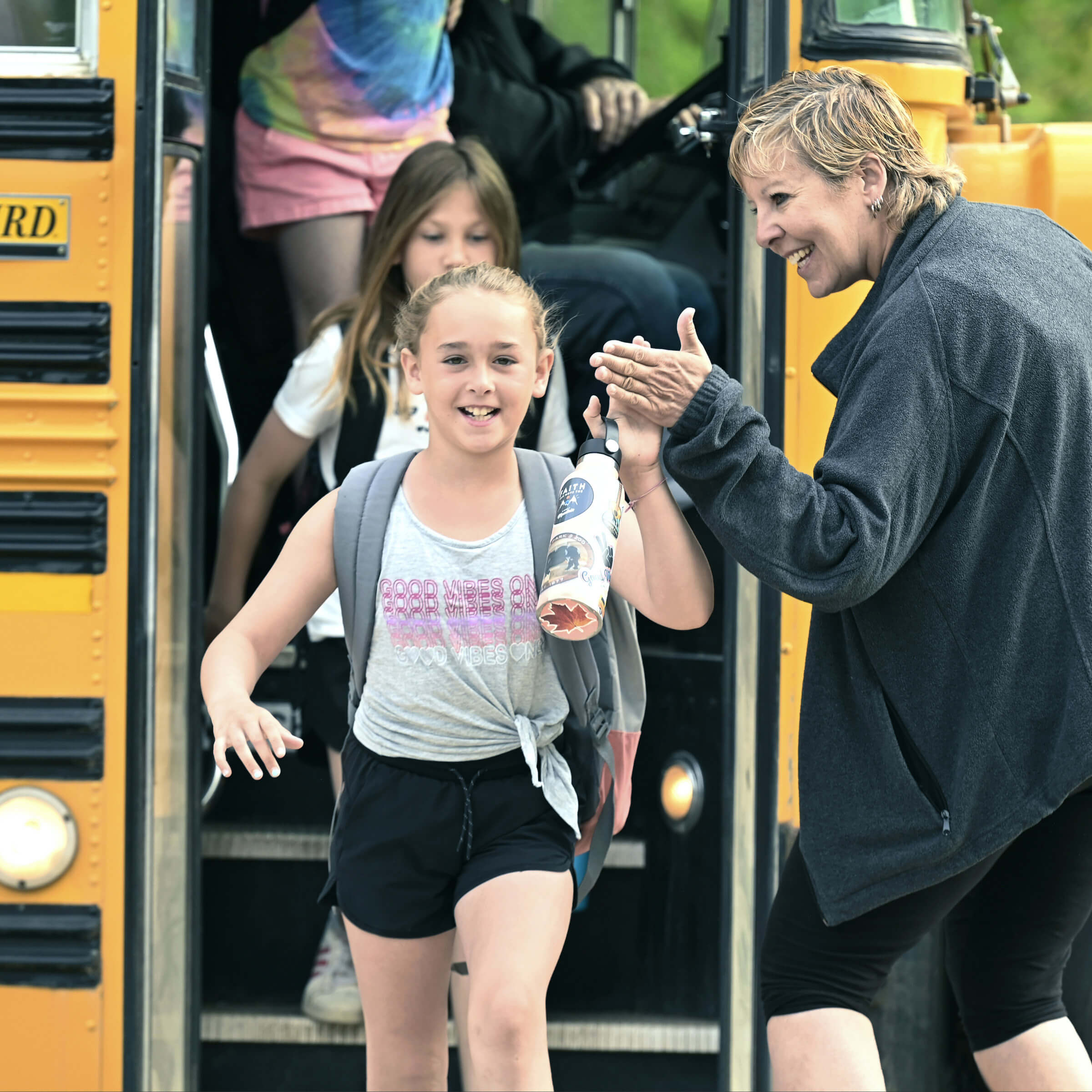 A teacher giving a high five to a child who is getting off of a school bus.
