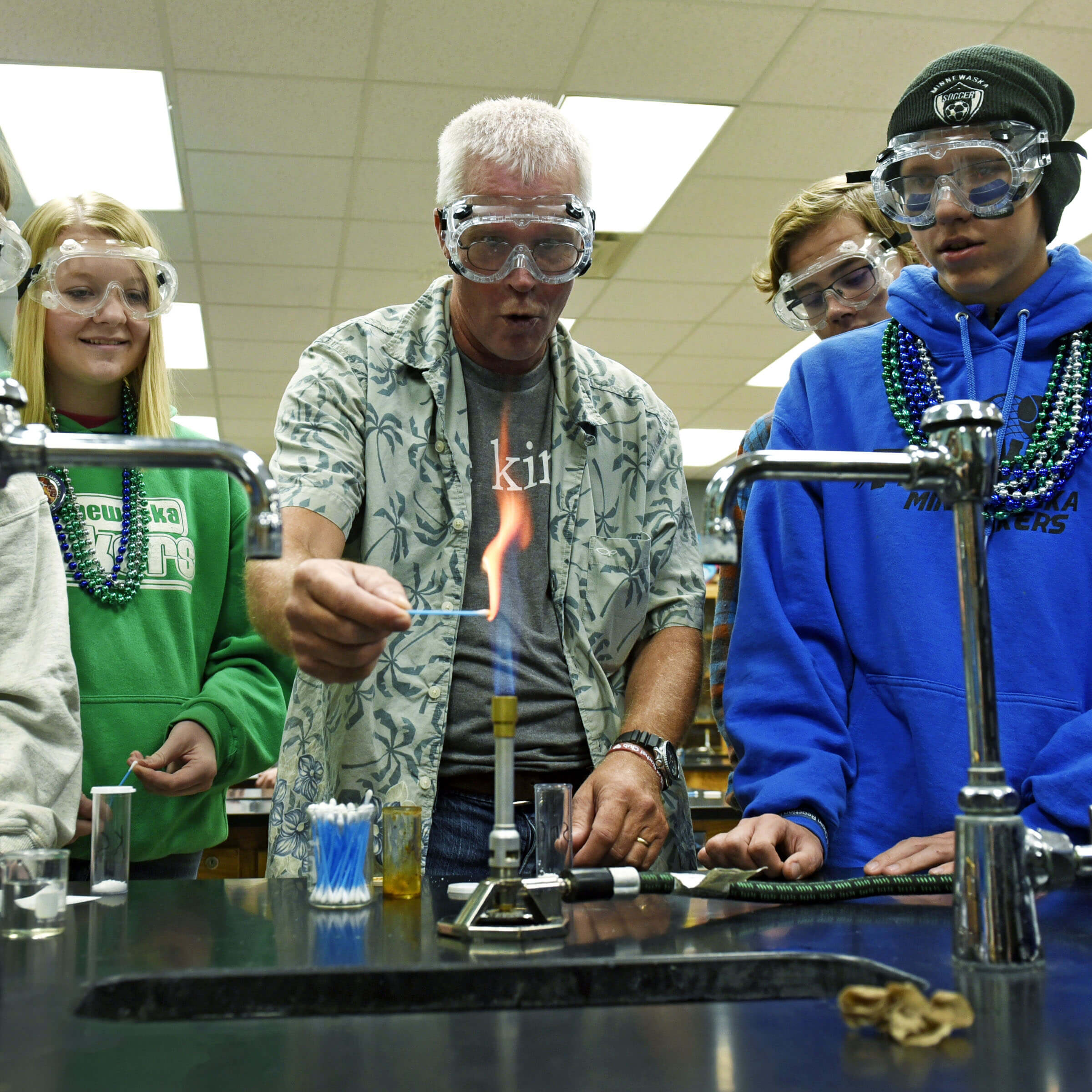 A teacher and three students wearing safety goggles during a science experiment.