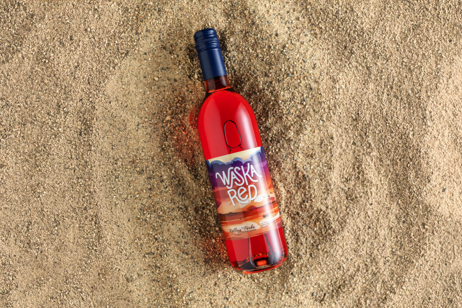 Red wine bottle laying in the sand